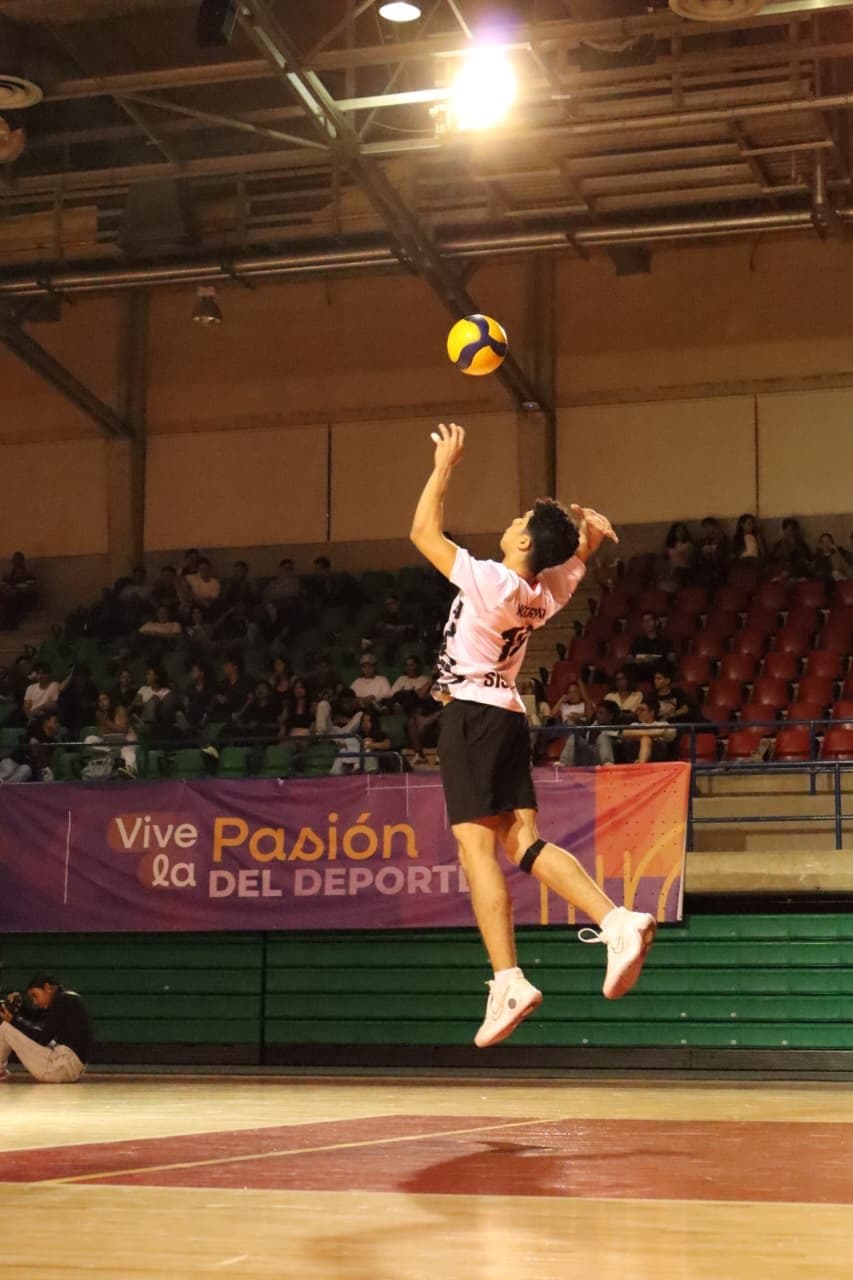 Andrés jumping to serve a volleyball in an indoor court